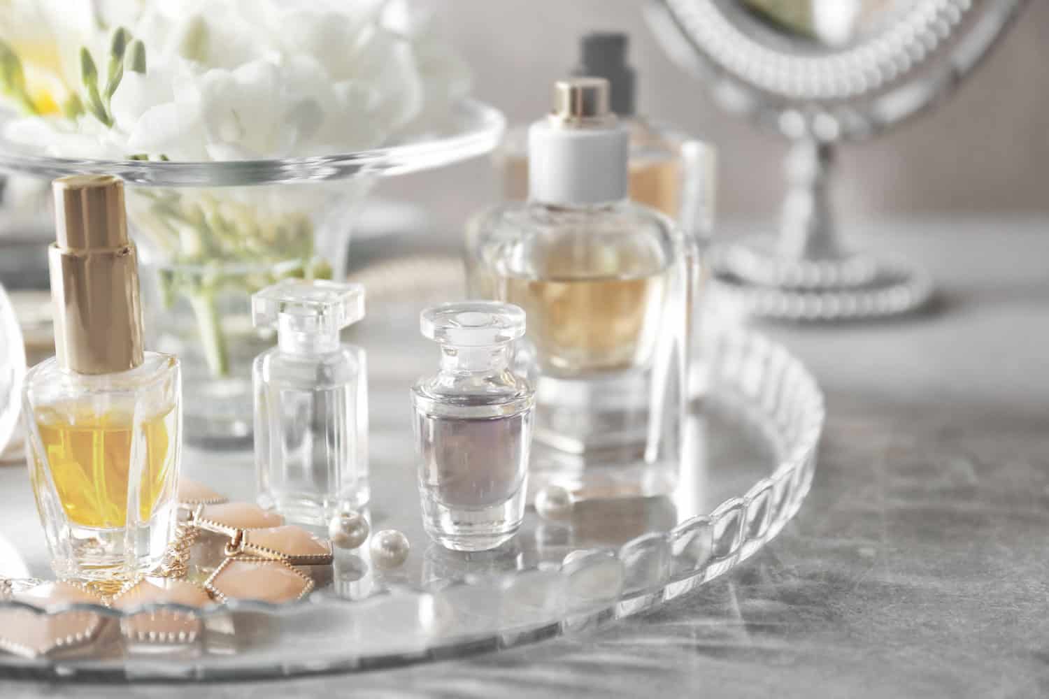 Plateau en verre avec des flacons de parfum sur une table grise